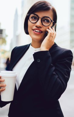 Ciddi bir şirket yöneticisi kahve molası sırasında telefonda konuşuyor. Elinde yemek fincanı, resmi giysili ve gözlüklü bir iş kadını iş arkadaşıyla gezici sohbetin keyfini çıkarıyor.