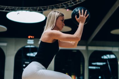 Siyah ve beyaz taytlı bir kadının spor salonunda spor yaparken başka tarafa baktığı yan görüntüler.