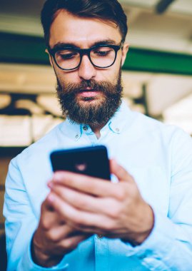 Cep telefonu multimedya uygulaması üzerinden SMS mesajı gönderen sakallı Kafkas hipster adam, gözlükler genç erkek Blogger hücresel Gadget üzerinden sosyal ağlar için yeni yayın oluşturma