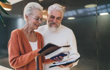 Kıdemli adam ve kadın belgeleri birlikte gözden geçiriyorlar, gülümsüyorlar ve tartışıyorlar. Her ikisi de profesyonel bir ortamda işbirliğini, deneyimi ve olumlu etkileşimi sembolize eden günlük kıyafetler giyiyordu.