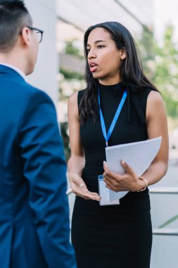 Kağıtları tutan ve iş konferansı düzenlerken erkeklerle konuşan zarif Afrikalı Amerikalı kadın sokakta duruyor.