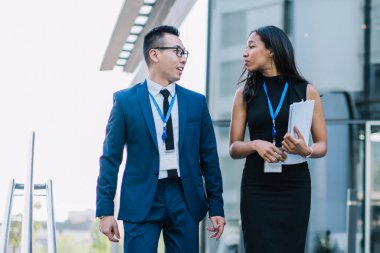 Asyalı erkek meslektaşı olan zarif Afrikalı Amerikalı iş kadını modern konferans sırasında elinde belgelerle merdivenlerde yürüyor.