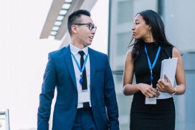 Asyalı erkek meslektaşı olan zarif Afrikalı Amerikalı iş kadını modern konferans sırasında elinde belgelerle merdivenlerde yürüyor.