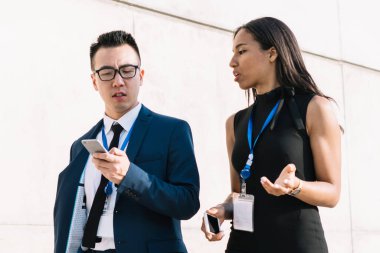 Modayı takip eden çok ırklı kadın ve erkek kimlik kartlarıyla sokakta yürüyor cep telefonlarını paylaşıyor ve gün ışığında tartışıyorlar.