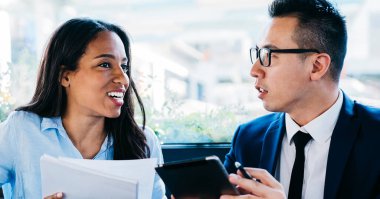 Modern kafede masa başında oturmuş iş projelerini tartışan çok ırklı kadın ve erkek aletler.