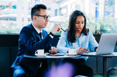 Modern etnik kadın ve erkek kafeteryada toplanıyor iş toplantısı yapıyorlar ve konuşurken dizüstü bilgisayar kullanıyorlar.