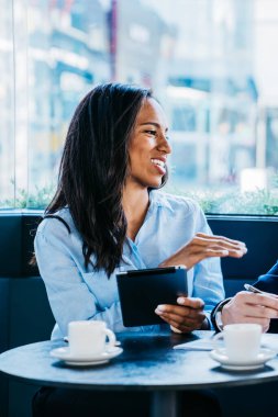 Modern çok ırklı kadın ve erkek kafeteryada kahve fincanları ve zımbırtılarla oturuyor ve iş projesi hakkında tartışıyorlar.