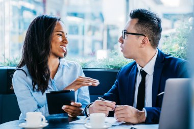 Modern çok ırklı kadın ve erkek kafeteryada kahve fincanları ve zımbırtılarla oturuyor ve iş projesi hakkında tartışıyorlar.