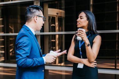 Çağdaş Afro-Amerikan kadın ve Asyalı erkek sokakta yan yana durup konferans sırasında kahve içiyorlar.