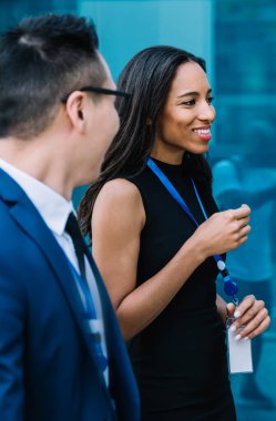 Afro-Amerikan kadın ve takım elbiseli adamın yan görünüşü. İsim etiketi takıyor ve boş zamanlarında sokakta yürürken konuşuyor.