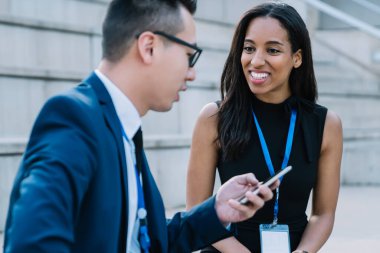 Asyalı erkek iş arkadaşı olan neşeli, genç bir etnik iş kadını. Konferans sırasında sohbet ederken sokakta oturuyor ve cep telefonunu paylaşıyor.