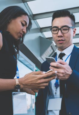 Şehir tren istasyonunda yan yana durup sohbet ederken cep telefonu kullanan, isim etiketli çağdaş kadın ve erkek.