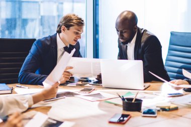 Dizüstü bilgisayarla çalışan genç kadın ve erkek grupları ve çeşitli evraklar ve fotoğraflar takımda yeni projeler yaratıyor.