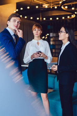 Bir grup gülümseyen zarif kadın ve takım elbiseli genç adam modern ofis koridorlarında boş boş sohbet ediyorlar.