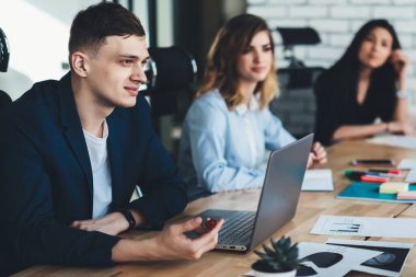 Genç erkek ve kadın iş arkadaşları modern ofis planlama şirketinin finans tarafında birlikte çalışıyorlar, zeki ortaklar masada oturuyor ve üretken iş stratejileri hakkında tartışıyorlar.