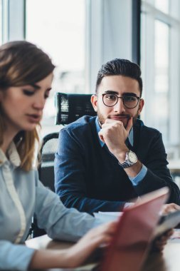 Yeni açılan bilişim projesi için bilgi toplayan erkek ve kadın meslektaşlar kameraya bakarken, optik gözlüklü beyaz iş adamının portresi göz koruması sağlıyor.