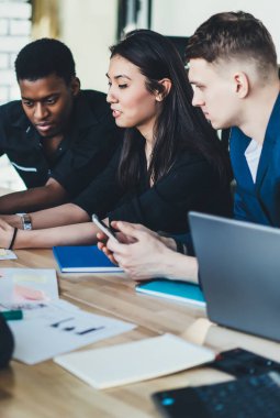 Bir grup genç perspektif çalışanı, ofis masasında otururken ve iş birliğinin keyfini çıkarırken modern cep telefonunda 4G bağlantısı kullanarak bir sonraki proje hakkında patrondan e-posta okuyor.