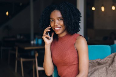 Çekici koyu tenli dişi, kafeteryada dinlenmek ve mobil uygulama, iletişim konsepti ile dostça konuşma yapmak için vakit geçirmek için el kafein içeceğiyle portre