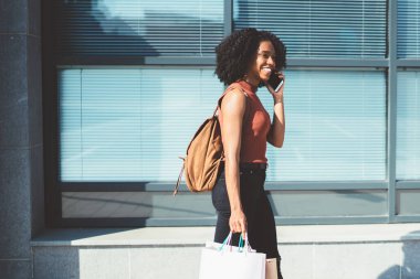 Modern akıllı telefon cihazında dolaşım internet bağlantısı kullanarak siyah Cuma sırasında iyi satın alma övünme için en iyi arkadaşa arayan elleri sırt çantası ve alışveriş torbaları ile neşeli hipster kız