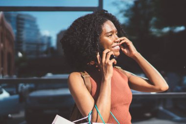 Neşeli koyu tenli hipster kız kıvırcık saç şehir alışveriş süresi sonra uluslararası akıllı telefon konuşma zevk ile, olumlu kadın genç gülümseyen mobil uygulama ile iletişim sırasında