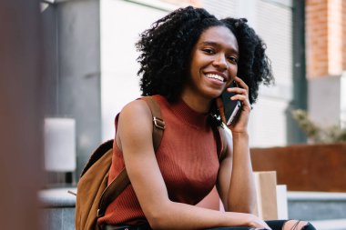 Mobil uygulama ile iletişim sırasında kamera gülümseyen Casual giyim giyinmiş neşeli kadın öğrenci portresi, hücresel gezici bağlantı kullanarak pozitif milenyal siyah model