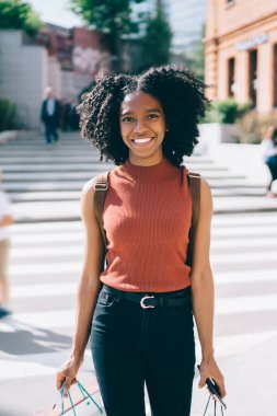 Yarı uzunluklu portre neşeli kadın genç rahat giyim kentsel ayarı ayakta giyinmiş ve şehirde güneşli yaz havalarda kamera gülümseyen, Genç koyu tenli bin kavramı