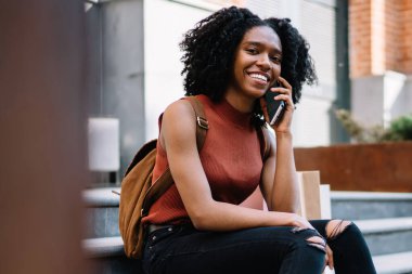 Mobil uygulama ile iletişim sırasında kamera gülümseyen Casual giyim giyinmiş neşeli kadın öğrenci portresi, hücresel gezici bağlantı kullanarak pozitif milenyal siyah model