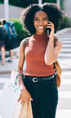 Yarım boy mutlu hipster kız portresi Siber Pazartesi satışlarında iyi alışverişler yaptıktan sonra heyecanlanıyor. Detayları konuşmak için arıyor. Elinde kağıt torbalarla kameraya gülümseyen neşeli kadın.