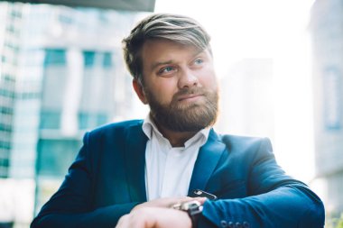 İş hayatı tarzında dalgın sakallı bir erkek ofis çalışanının kol saati kullanırken ve bulanık arka plana bakarken giydiği kontrol çizelgesinden.