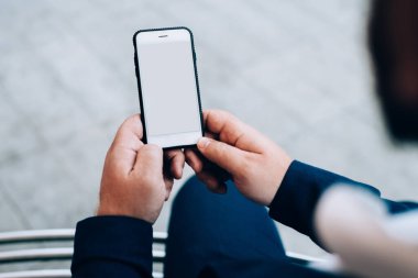 Yukarıdaki cep telefonundan, asfalt yolda otururken çalışan koyu renk elbiseli bir mahsul.