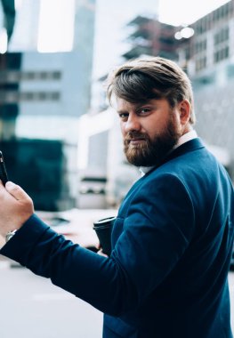 Ciddi bir adamın elinde telefonla arka planda şehir trafiğinin arka planındaki kameraya bakması.