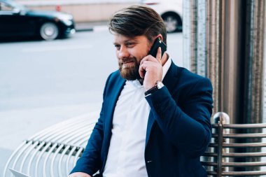 Gündüz vakti kalabalık bir caddenin ortasında otururken elinde dizüstü bilgisayarla telefonla konuşan tatmin olmuş bir adam.