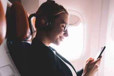 Neşeli kadın yolcu yan görünümü eğlenceli metin gemide WiFi bağlı, pozitif kız gürültü iptali için kulaklıkta müzik zevk ile alınan dostu mesaj iyi hissediyor