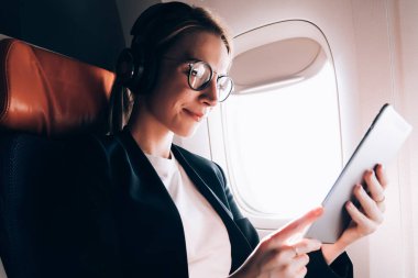 Çekici kafkas kadın yolcu uçak içinde kıtalar arası uçuş sırasında modern dokunmatik yüzey üzerinde WiFi internet bağlı, kulaklık kadın dijital tablet uygulama yoluyla film izliyor