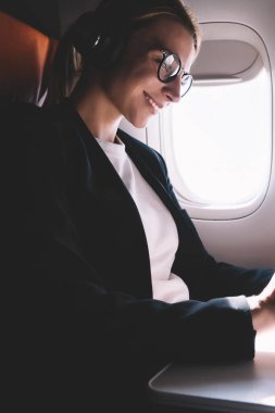 Rahatlatıcı uçuş sırasında dijital tablet üzerinde gemide WiFi internet bağlı arkadaşınıza metin mesajı yazarak neşeli kadın yolcu. Uçak müzik dinleme mutlu kadın turist, kablosuz hizmet