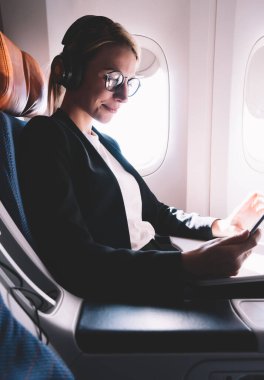 Gemide WiFi bağlı Kıtalararası uçuş sırasında sosyal ağda vizyon düzeltme okuma metin yayınları için gözlük pozitif beyaz kadın, mutlu kadın tarama web siteleri