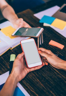 Modern iş arkadaşları boş ekranlı cep telefonlarına göz atarken ve tartışırken kağıt ve defterlerle masada toplanıyor.