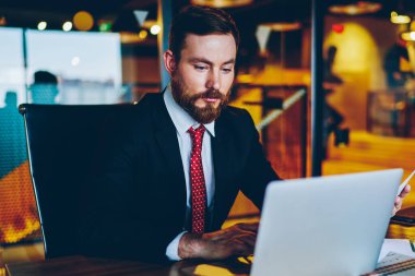 Ofis iç masada otururken modern dizüstü bilgisayar veritabanında veritabanı uygun online klavye bilgi giyinmiş sakallı gururlu CEO 'su. Netbook üzerinde Pensive işadamı online klavye e-posta