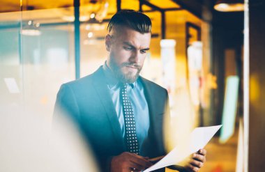 Kağıt belgesinden mali raporların bilgi okuma uygun giyinmiş Pensive sakallı başarılı girişimci. İş işadamı ofis iç ayakta muhasebe belgeleri kontrol