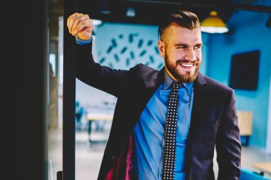 Resmi giyim giymiş başarılı sakallı işadamı kendi yeni modern ofis iç kendine güvenen ve heyecanlı hissediyorum. Uzağa bakarken gülme 30 yıl eski erkek girişimci gülüyor