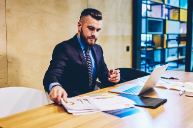 Şık takım elbise kontrol belgeleri ve modern dizüstü bilgisayar cihazı kablosuz internet kullanarak online veritabanı giymiş müreffeh akıllı işadamı. Başarılı gurur CEO 'su dijital Netbook çalışıyor