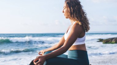 Spor eşofmanlı siyahi bir kadın, yoga eğitimi sırasında enerji seviyelerini ve farkındalığı düzeltir. Çekici aktif kız aydınlanma ve huzur için Padmasana zamanının tadını çıkarır.