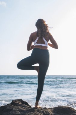Sağlıklı yaşam tarzı egzersiz kavramı - çıplak ayaklı kadın denge yoga yapıyor. Okyanus batımına yakın Vrikshasana, eşofman altı giymiş kızın ağaçtan poz verişi ve tüm zihinler için.
