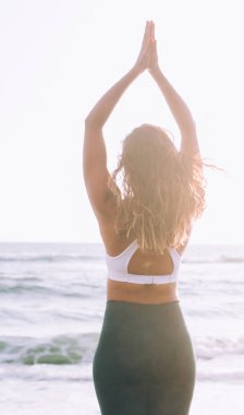 Elleri havada, dağ pozu veren genç sakin bir kadın kronik stres kalıplarını rahatlatmak için deniz sahilinde sabah antrenmanının keyfini çıkarıyor, maneviyat kavramı ve ruh ve zihin eğlencesi.