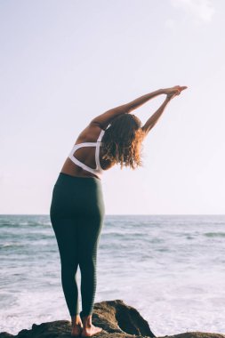 Genç bir kadın, vücut esnekliği ve kas esnekliği eğitimi için dağ yogası yapıyor. Spor eşofmanlı bir kadın, Asya okyanusu yakınlarında meditasyon yaparken ruhani ruh ve zihin.