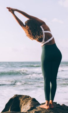 Dağ pozuyla dinlenen sakin bir kadın, deniz sahilinde motivasyon ve ruhani antrenman için boş günün keyfini çıkarıyor, elleri havada, iribaş egzersizi yapan bir kız, tüm zihinleri rahatlatmak ve ruhsal uyum elde etmek için.