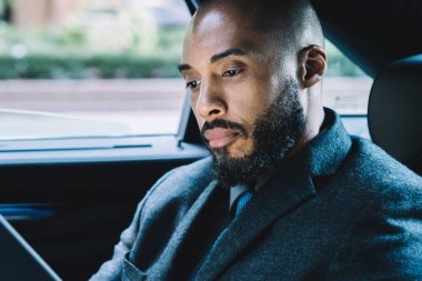 Siyah derili bir işadamı taksinin arka koltuğunda oturuyor ve modern dokunmatik ped üzerinden online video konferansı yapmak için iletişim numarasını arıyor. Tablette piyasa dijitalleşmesi kavramı.