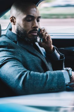 Ciddi Afrikalı Amerikalı bir adam iş ortağıyla buluşma yeri ve takılabilir kol saati için iletişim kuruyor. Resmi kıyafetli bir adam araba gezisi sırasında cep telefonu kullanıyor.