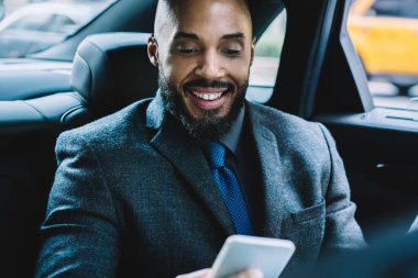 Başarılı sakallı adam elinde dijital bir alet tutuyor ve ofis arkadaşlarıyla mesajlaşırken gülümsüyor. Cep telefonuyla interneti taramak için 4G kablosuz ağ kullanıyor. Otomobildeki iş adamı.