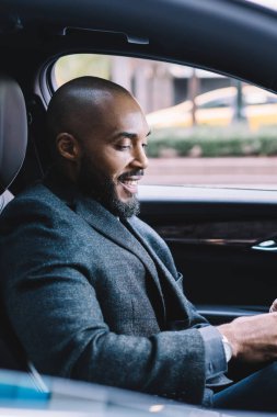 Postaları kontrol eden neşeli erkek bankacının yan görüntüsü. Arabada oturup sohbet etmek ve cep telefonu uygulaması üzerinden mesaj göndermek için mesaj yazan Afrikalı Amerikalı bir adama bağlanmak.